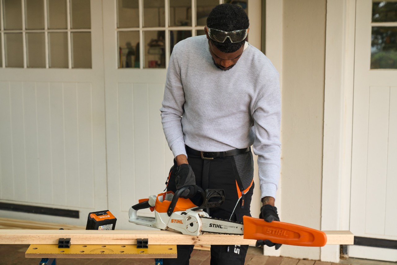 Мъж пред работилница сваля предпазителя на акумулаторен верижен трион STIHL MSA 70 