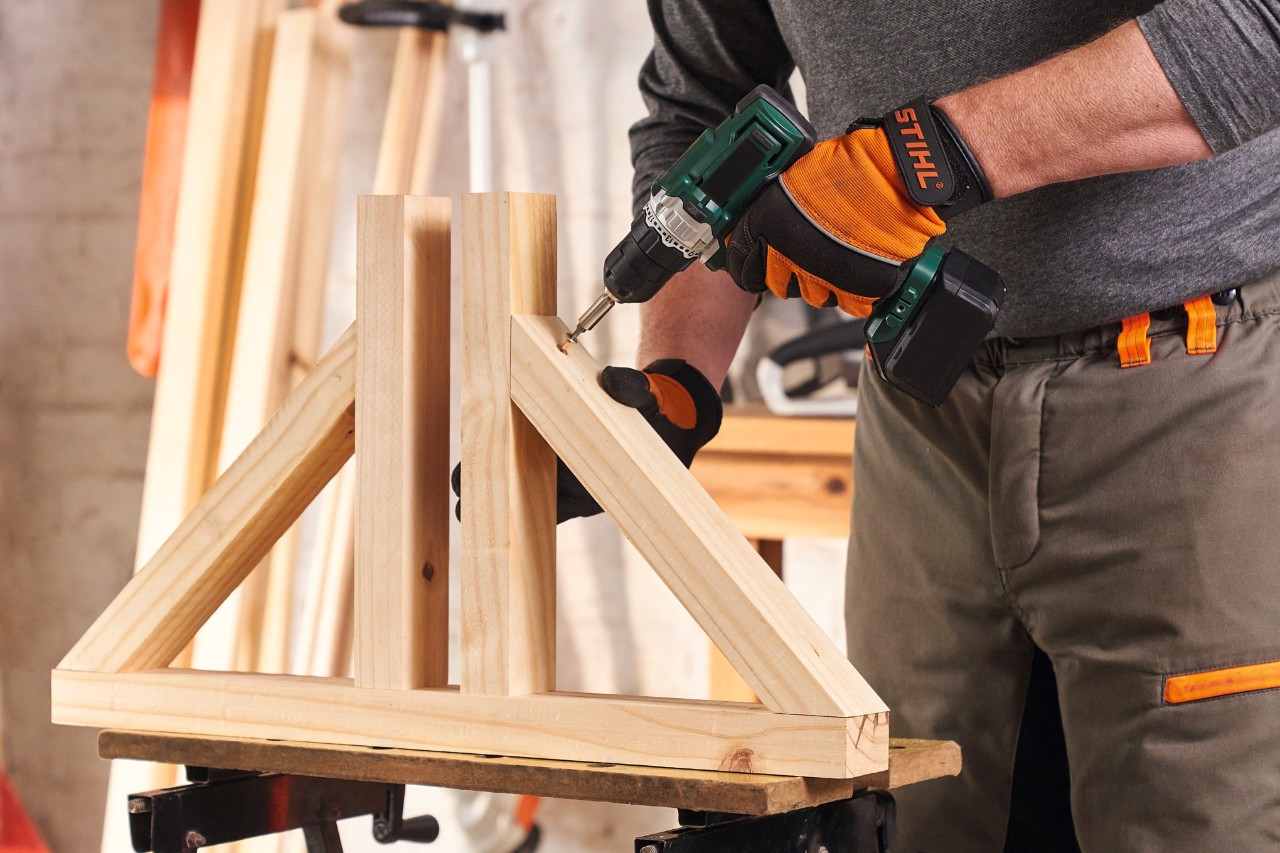 Човек със защитни ръкавици STIHL Function Protect завинтва стойките за дървена визуална защита