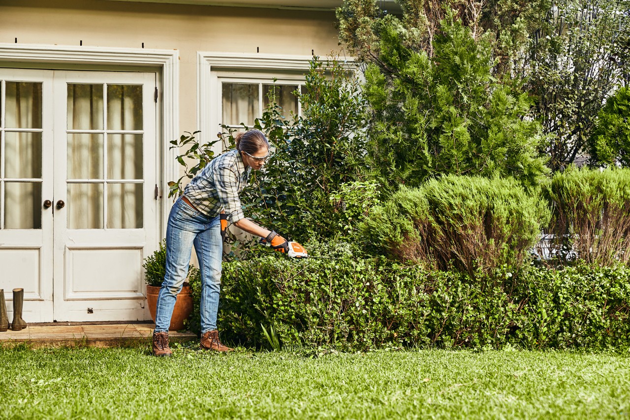 Жена подрязва жив плет от чемшир с акумулаторна ножица за жив плет STIHL HSA 26 пред бяла къща