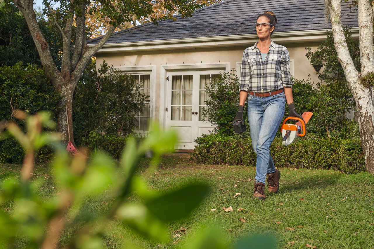 Жена минава през моравата пред къща с ножица за жив плет STIHL