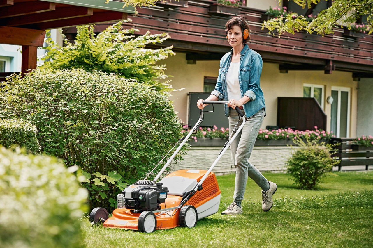 Жена се грижи за моравата през пролетта с бензинова косачка за трева STIHL RM 243 T в градината пред къща