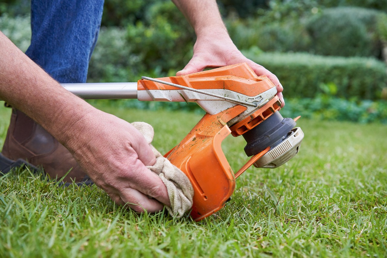 Човек почиства с влажна кърпа защитата на моторна косачка STIHL