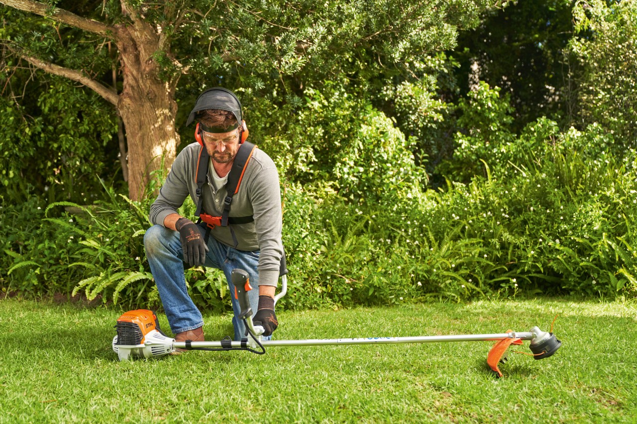 Мъж поставя бензиновата моторна косачка STIHL FS 91 на земята, за да я стартира