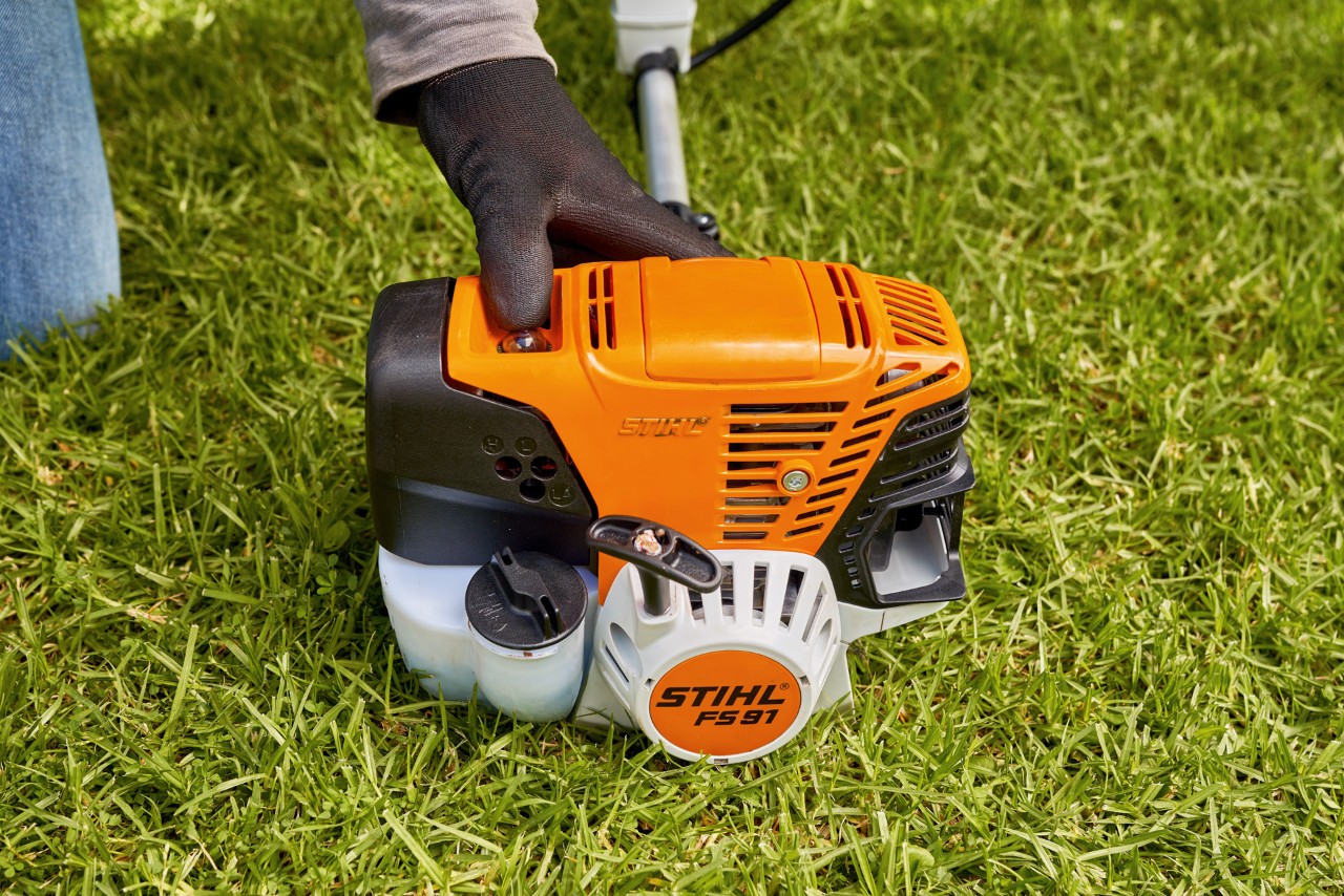 Мъж натиска горивната помпа на бензиновата моторна косачка STIHL FS 91, за да я стартира