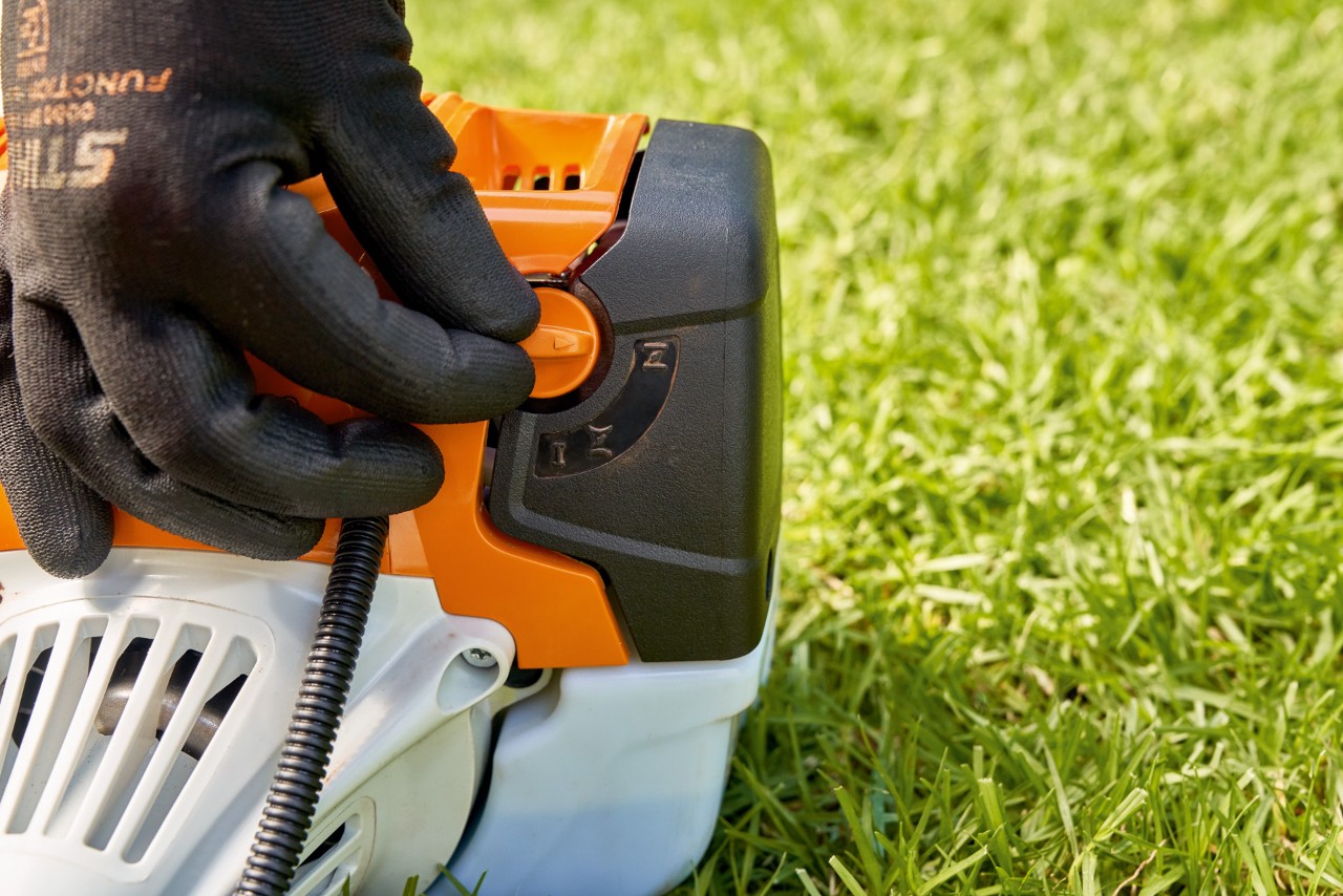 Мъж настройва лоста на горивната помпа на бензиновата моторна косачка STIHL FS 91, за да я стартира