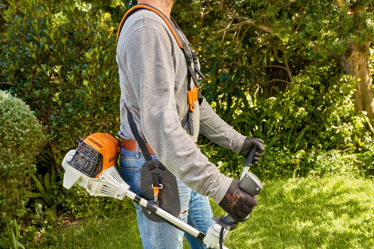 Мъж повдига бензиновата моторна косачка STIHL FS 91 от земята, за да стартира косенето 