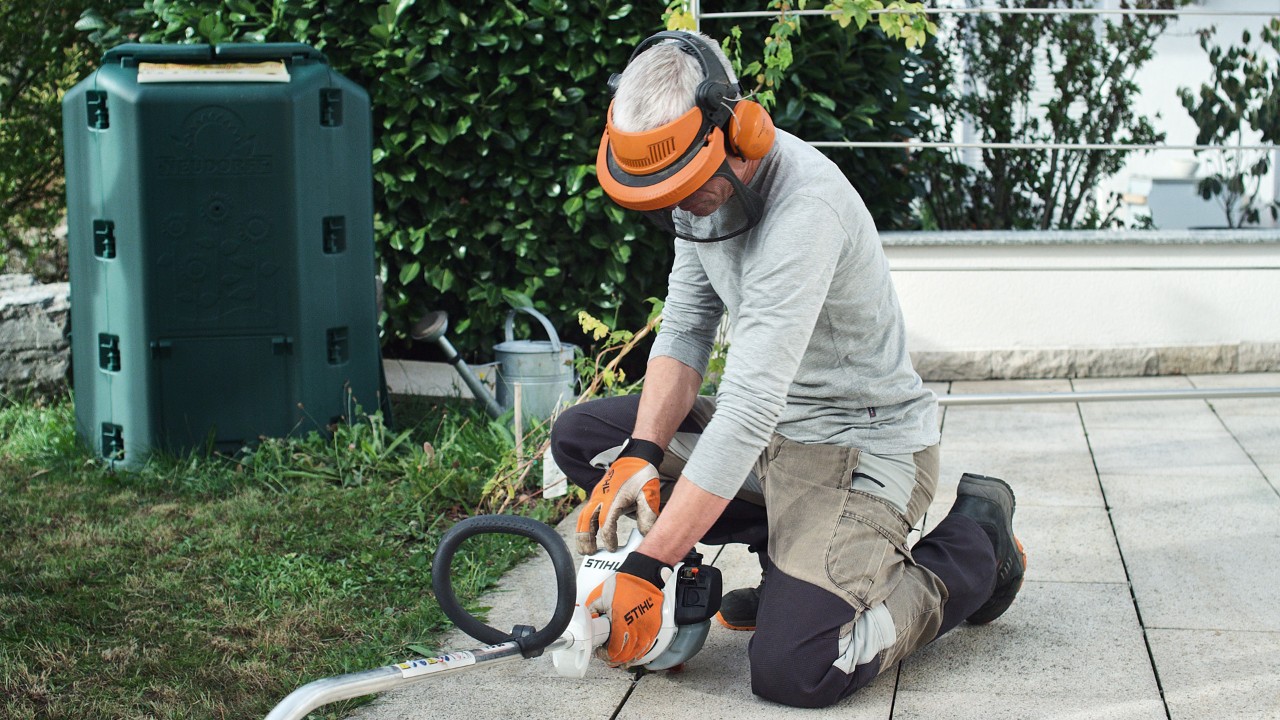 Бензиновата моторна косачка STIHL FS 38 се притиска на земята от човек в предпазно облекло