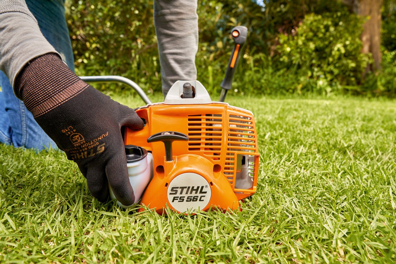 Мъж натиска горивната помпа на бензиновата моторна косачка STIHL FS 56, за да я стартира