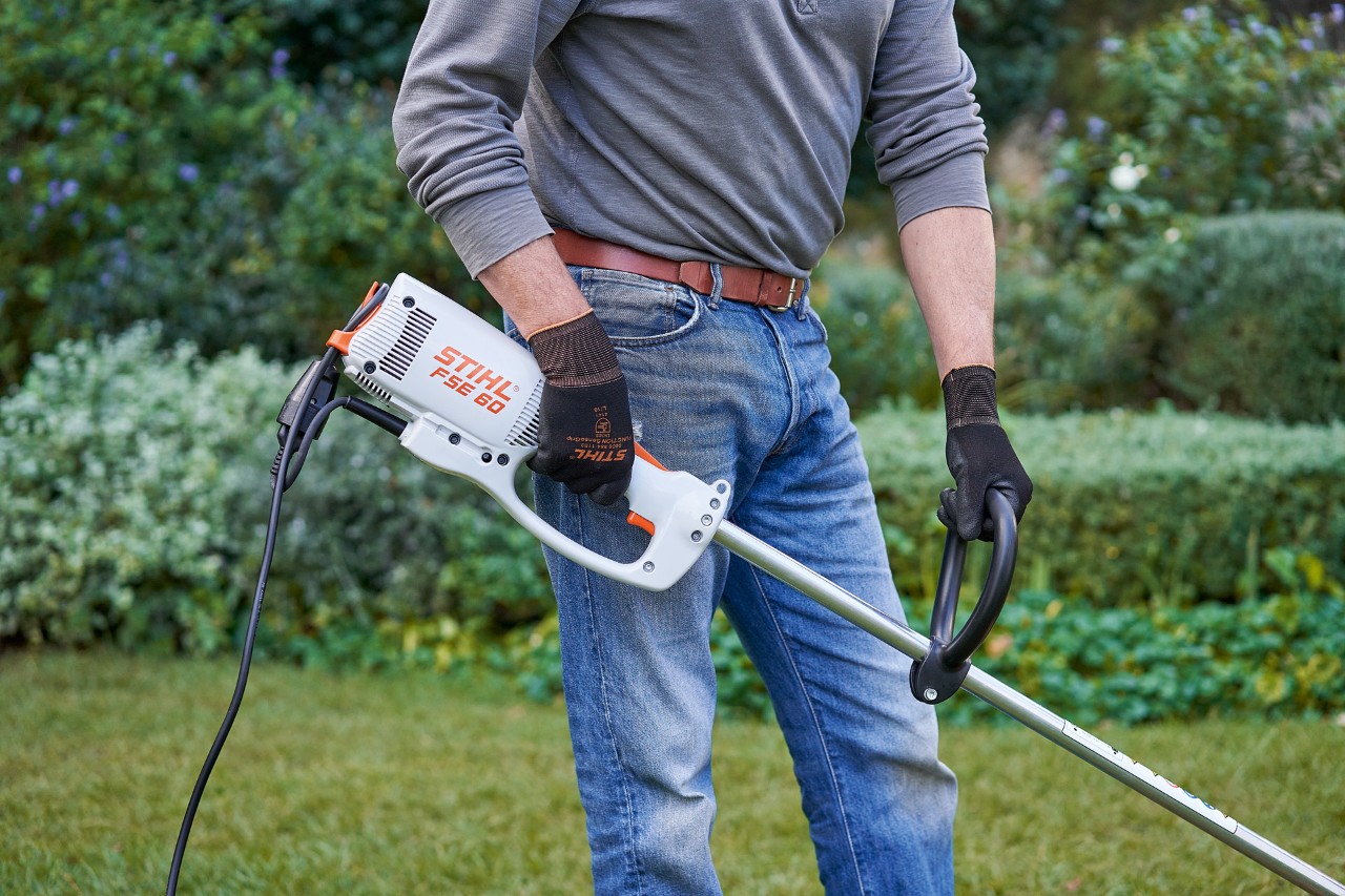 Мъж с предпазни ръкавици хваща електрическата моторна косачка STIHL FSE 60 с две ръце
