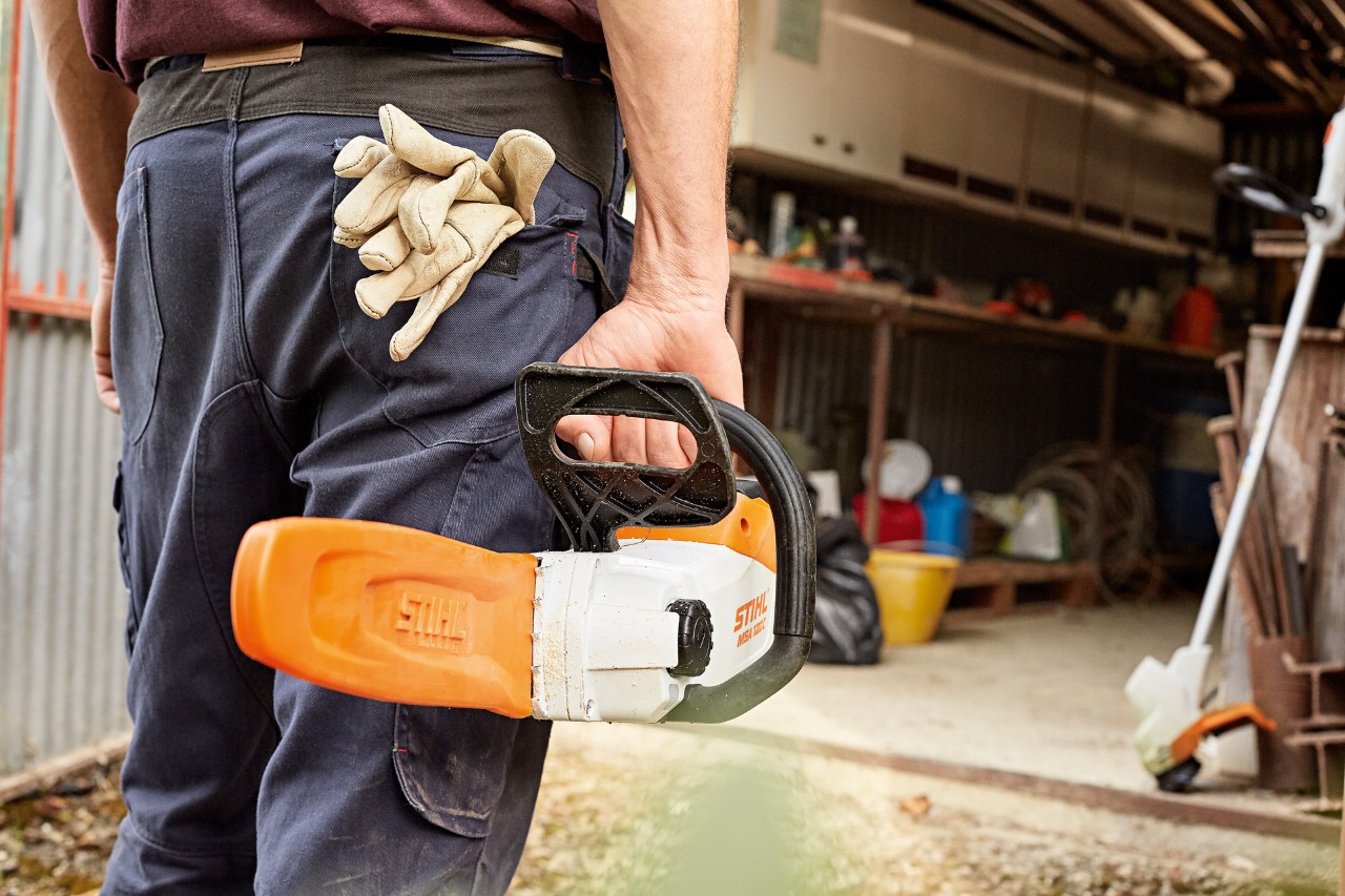 Мъж стои пред сервиз с акумулаторен верижен трион STIHL със защита на шината