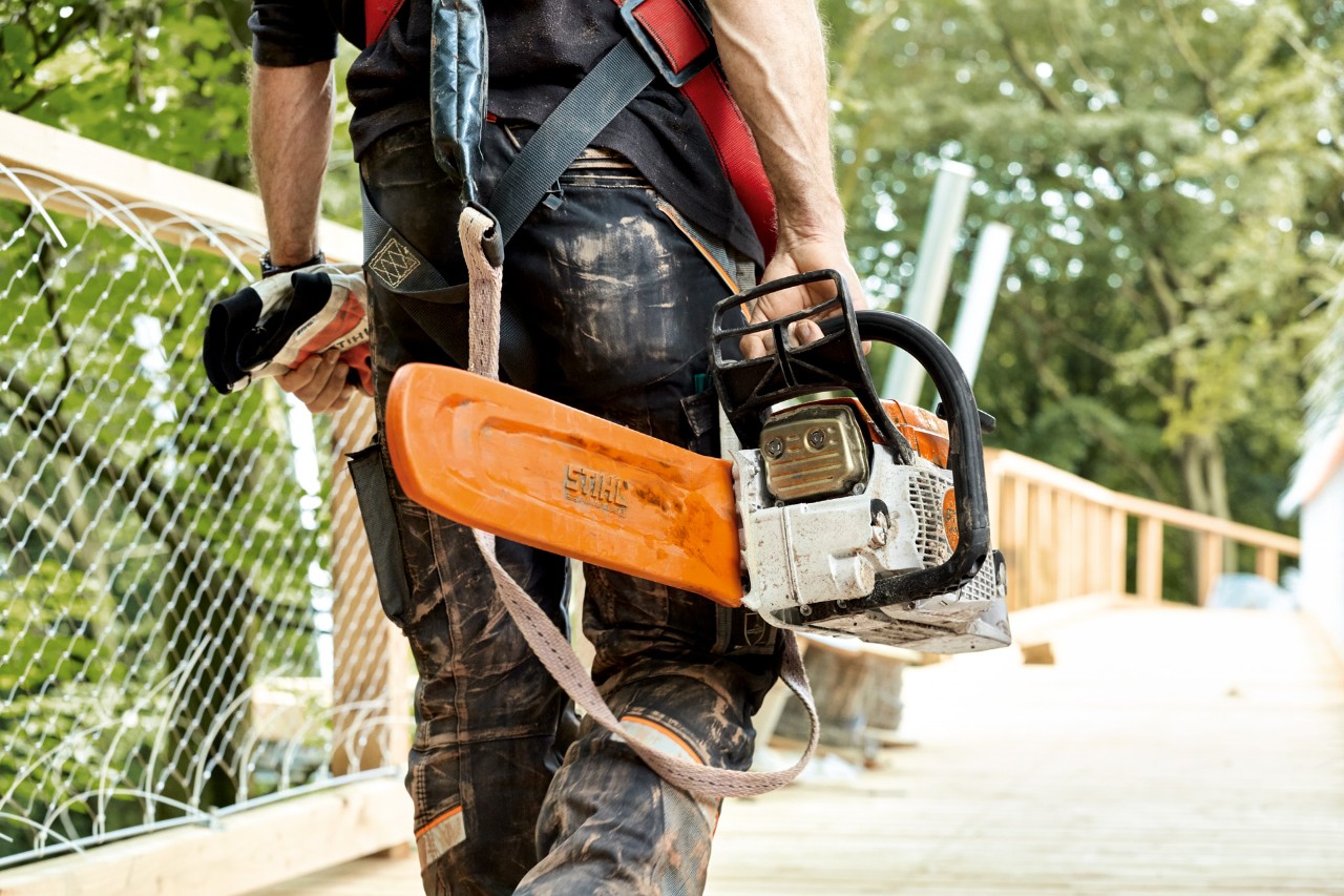 Мъж в защитно облекло носи бензинов верижен трион STIHL MS 261 с предпазител на веригата.