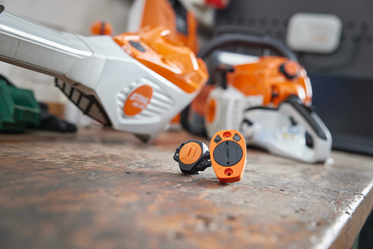 STIHL Smart Connector и STIHL Smart Connector 2 A се намират на работна маса. На заден фон се виждат нефокусирано различни уреди STIHL.