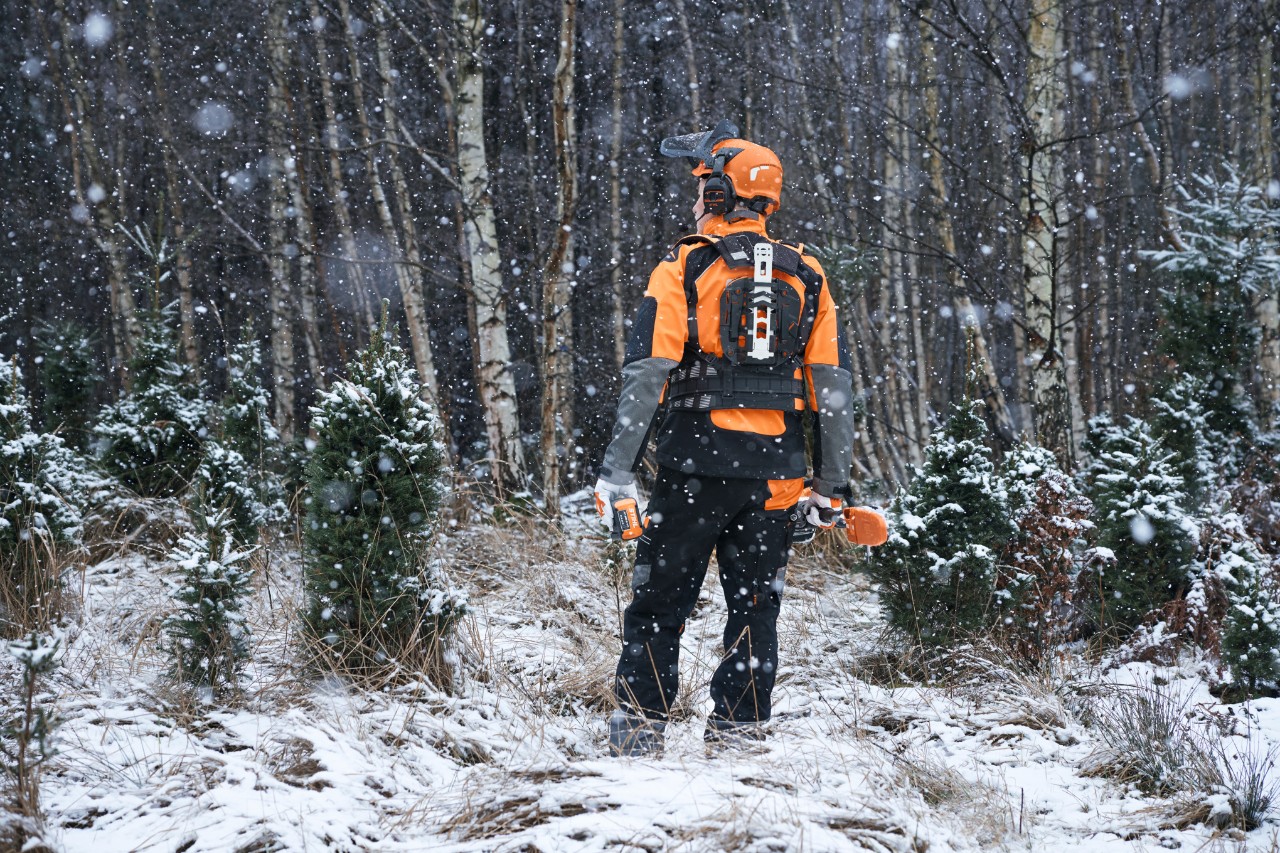 Горски работник в изглед отзад в заснежена гора, с предпазно оборудване STIHL с модулна система от колани и акумулаторни уреди за грижа за младите дървета