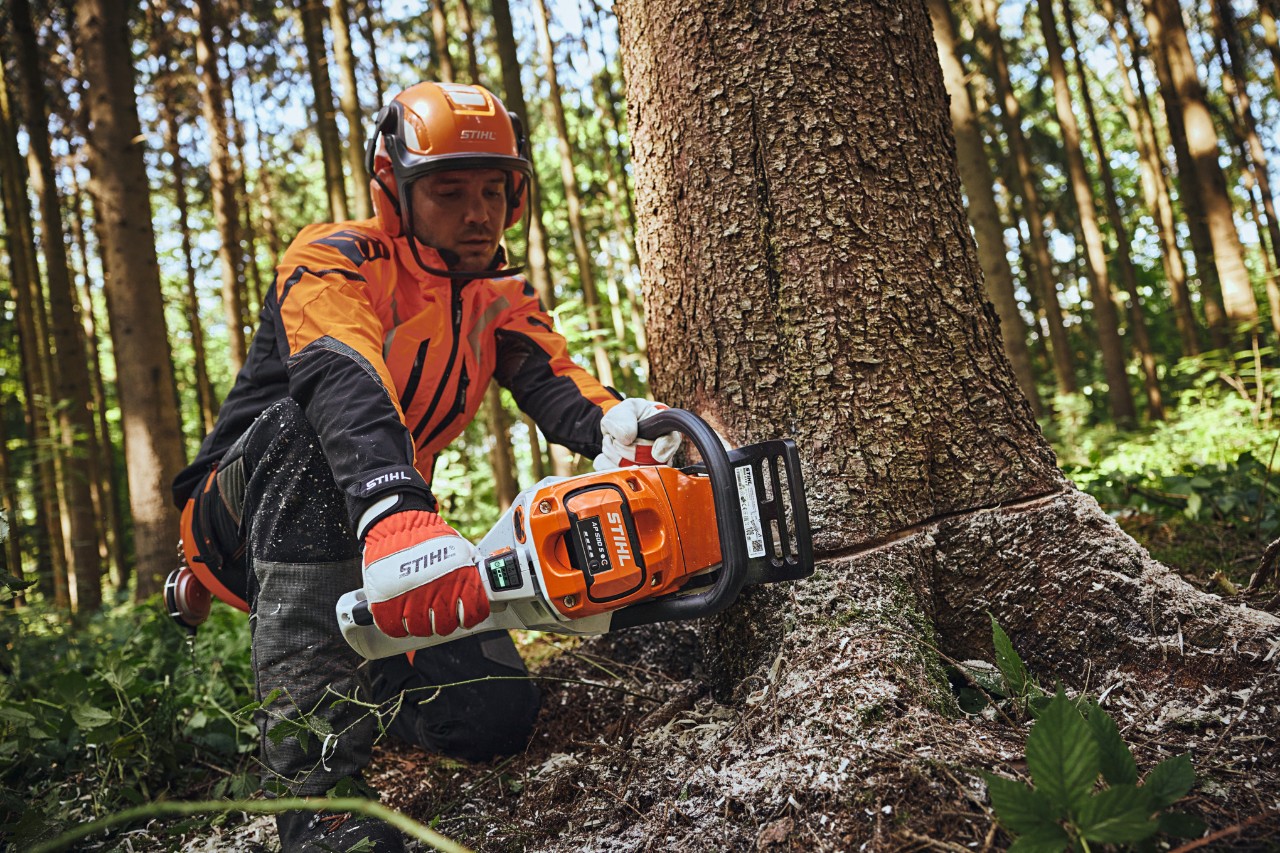 Мъж в лични предпазни средства STIHL реже дърво