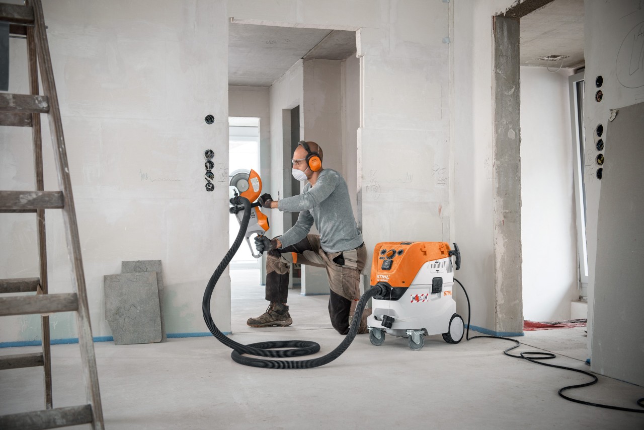Мъж използва прахосмукачка за сухо и мокро почистване STIHL SE 133 ME при работа с ъглошлайф STIHL TSA 230