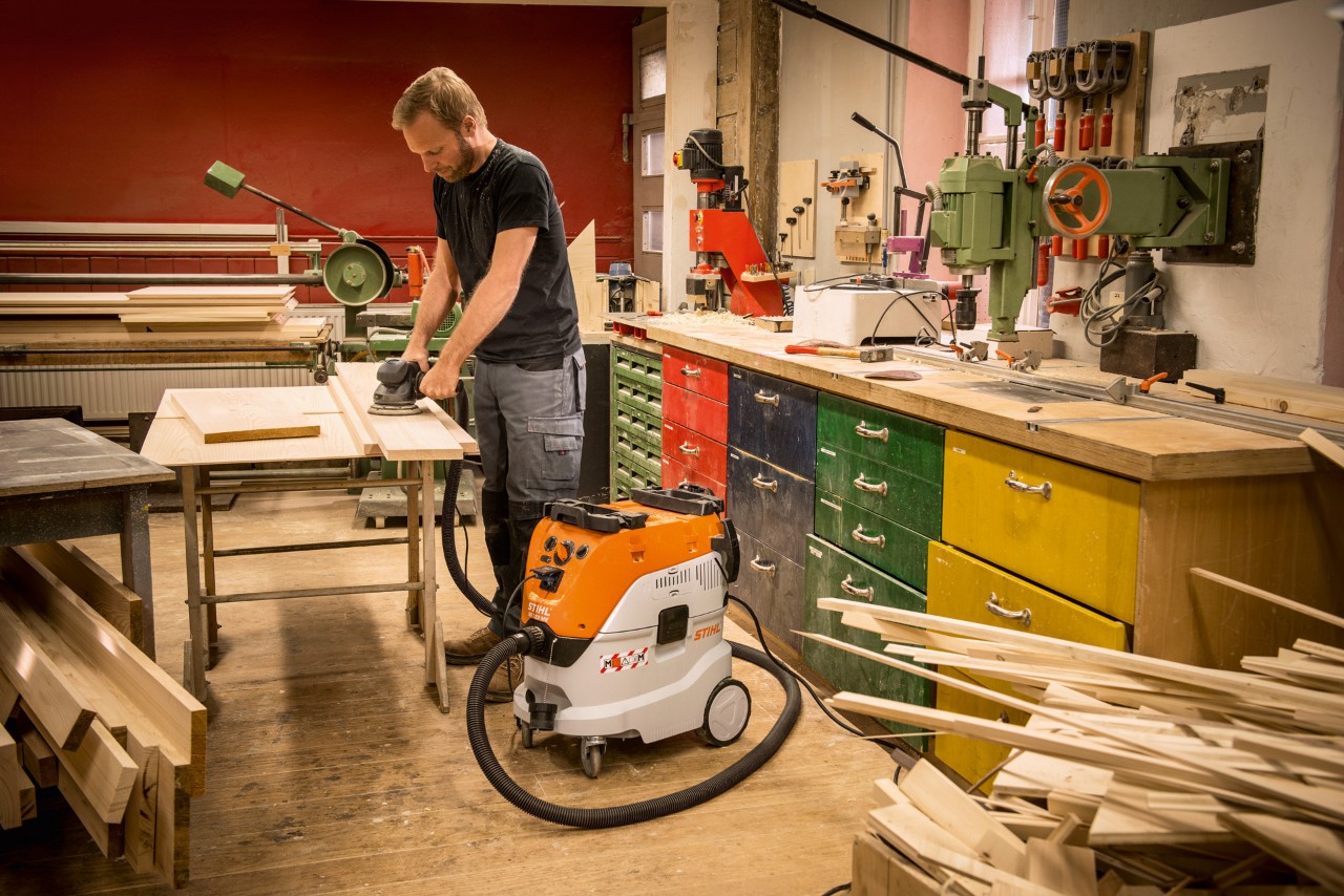 Мъж използва прахосмукачка за сухо и мокро почистване STIHL SE 133 ME в сервиз при работа с дървени дъски