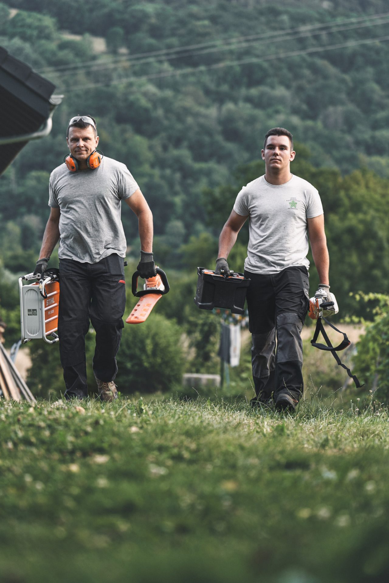 Двама професионалисти вървят по поляна с акумулаторни уреди STIHL
