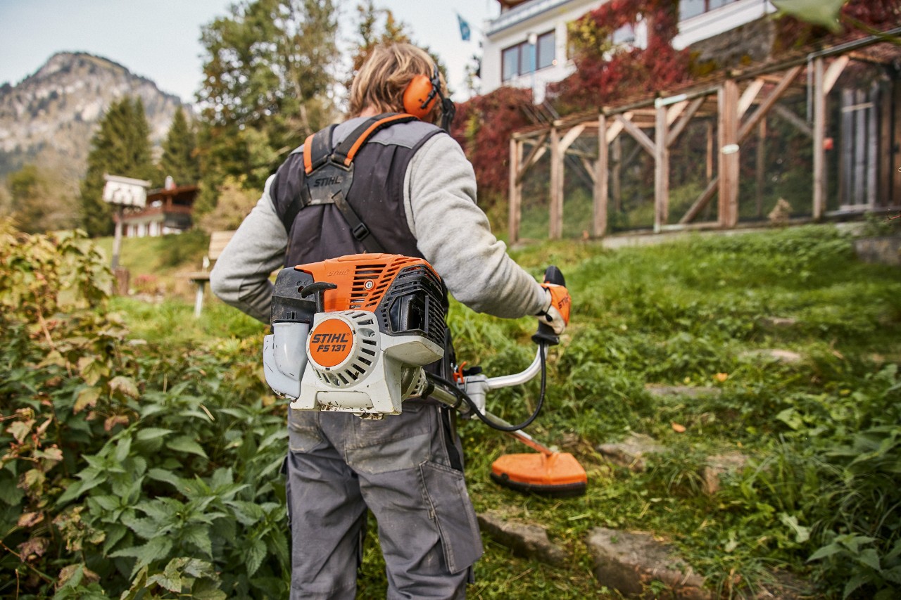 Стръмен терен пред къща се коси с бензиновата моторна косачка STIHL FS 131 с двигател 4-Mix®