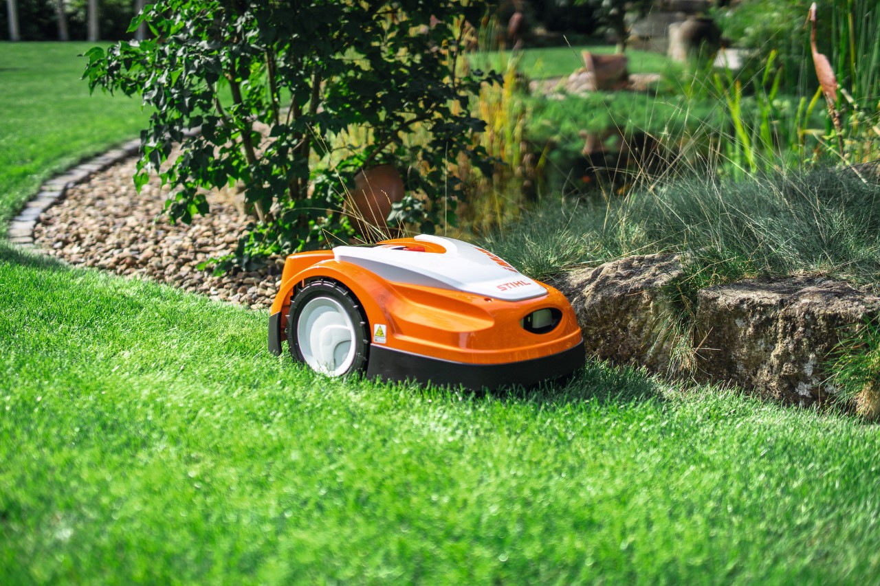 STIHL iMOW RMI 422 коси поляна в градината на края на малка каменна стена.