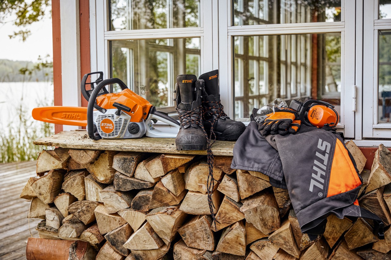 Предпазно облекло STIHL и MS 162 се намират на регал над куп дърва за горене