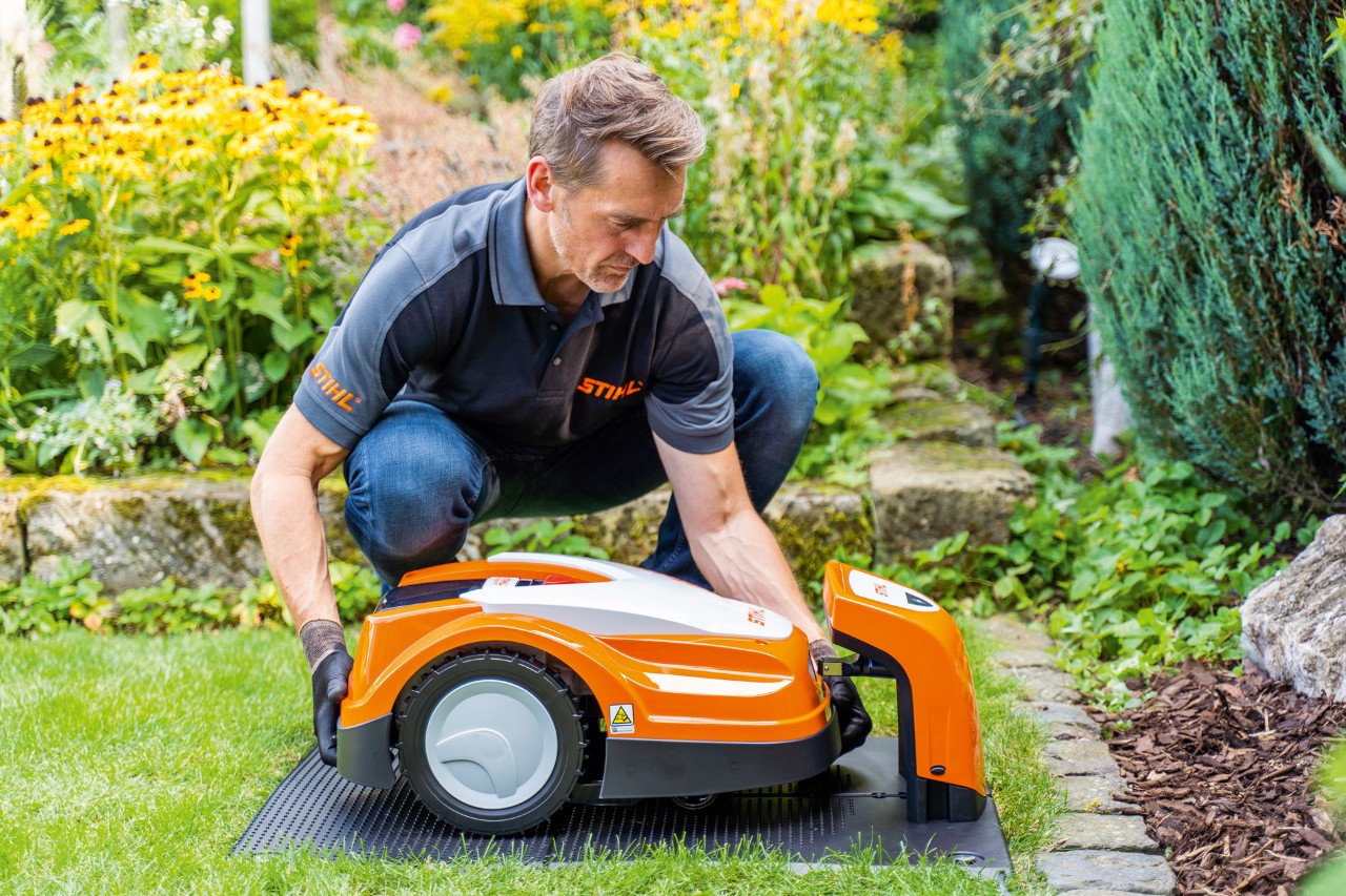 Специализиран дилър на STIHL поставя косачка робот STIHL iMOW в зарядната й станция в градина