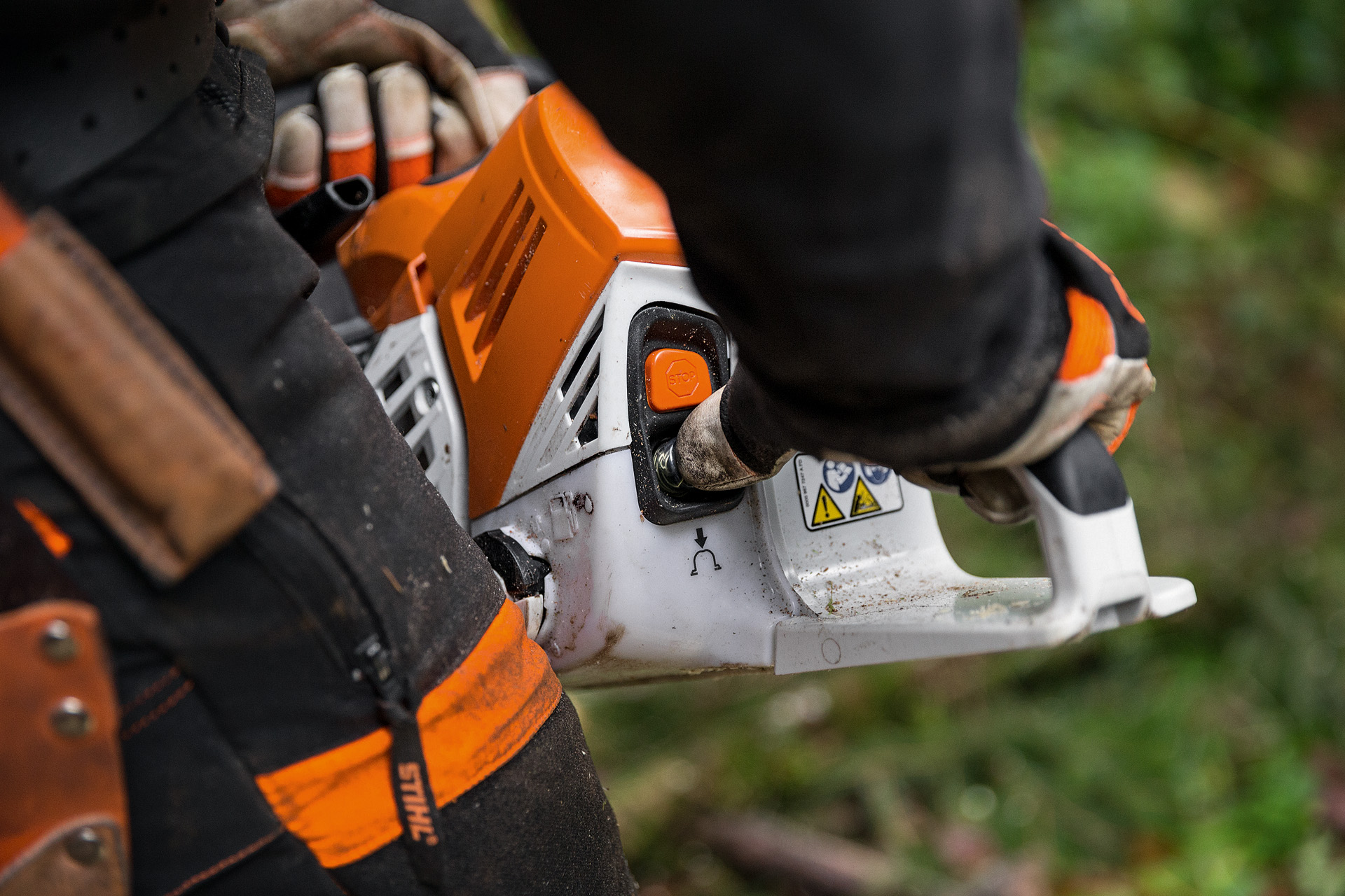 Човек в предпазно облекло стартира бензинов верижен трион STIHL MS 500i в разлистена гора на земята