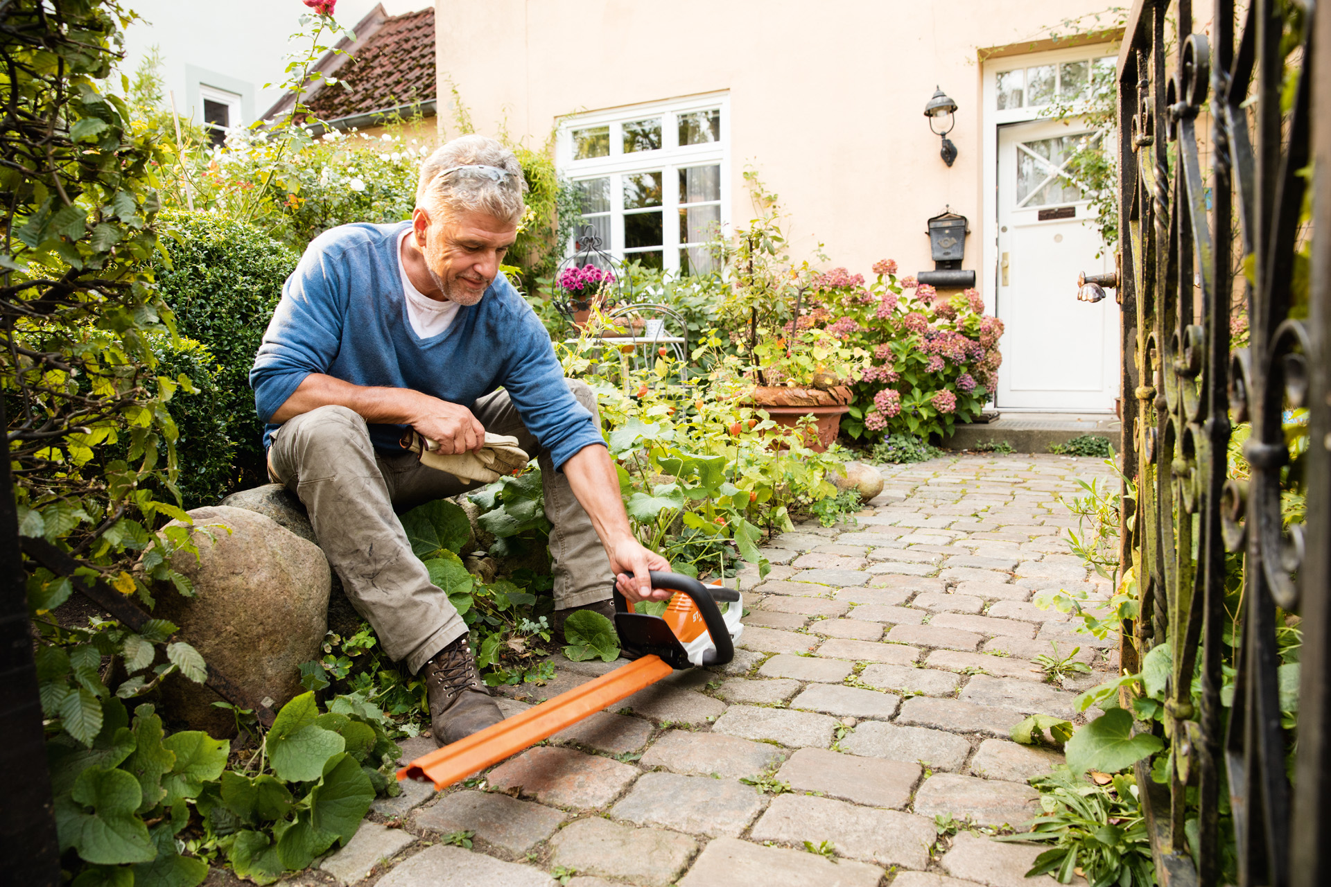 Мъж с електрическа ножица за жив плет STIHL HSA 45 от линията AI пред къща