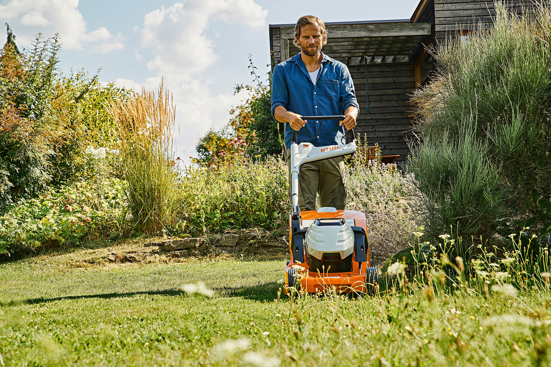 Мъж извършва грижа за моравата през лятото с акумулаторна косачка STIHL RMA 448 P-C върху имот с избуяла растителност